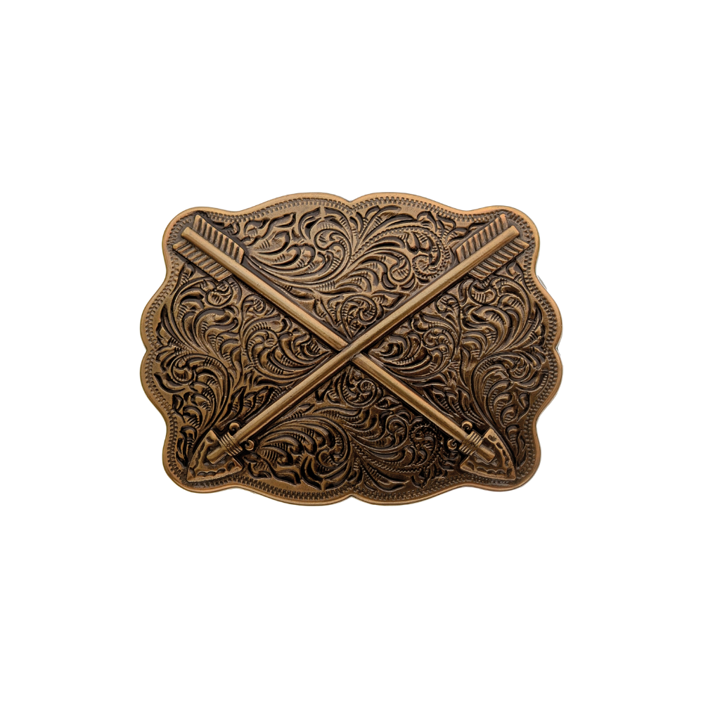 A detailed gold or bronze-toned belt buckle with a Western design. This fashion accessory features two crossed arrows over an ornate background of scrollwork and patterns.