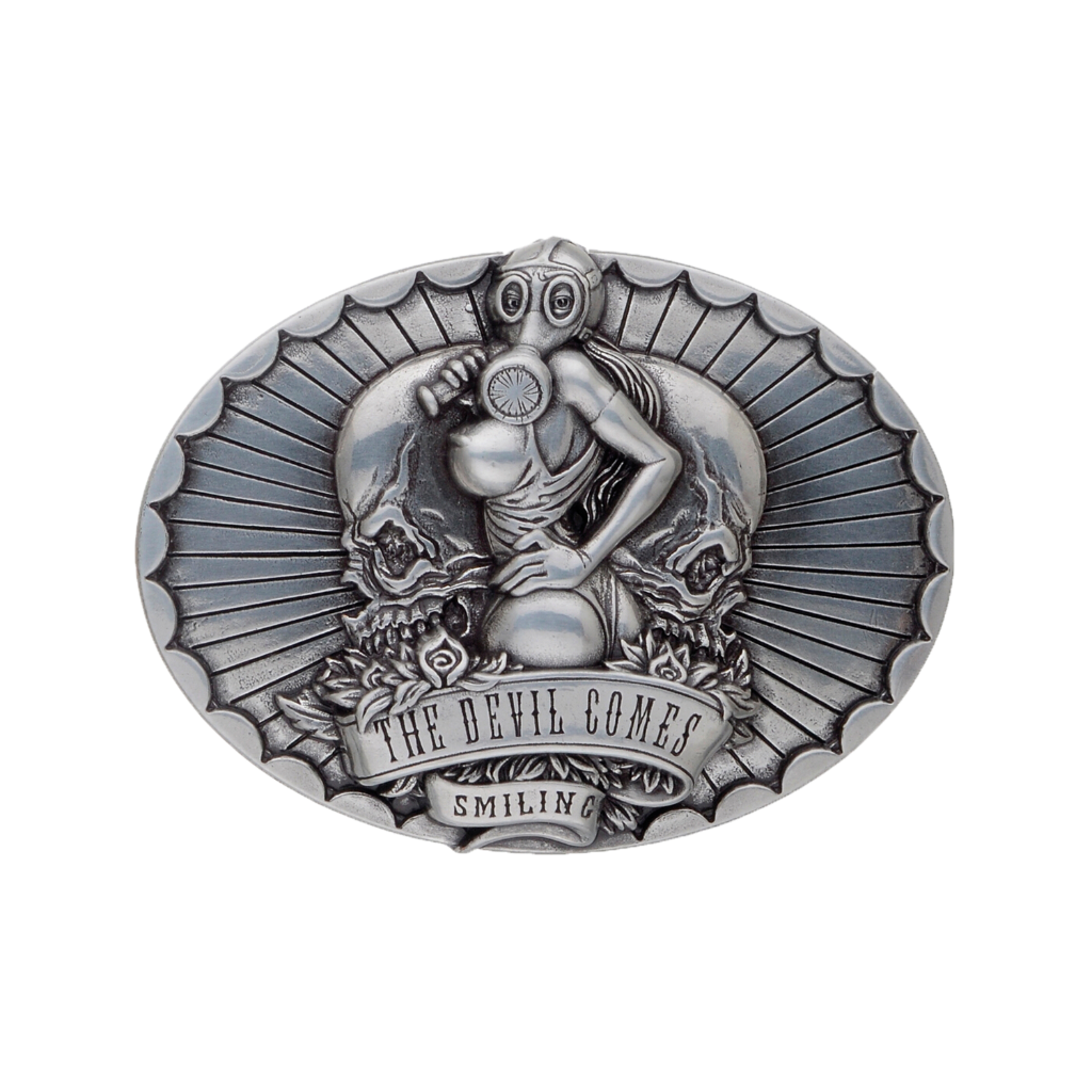 A detailed silver belt buckle with a gothic or biker-inspired design. This fashion accessory features a woman in a gas mask, a large skull, and a banner that reads 'THE DEVIL COMES SMILING'.